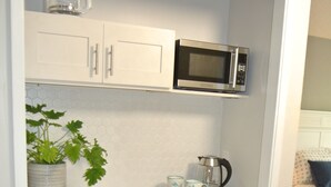 Un angolo cottura compatto dotato di forno a microonde, macchina per il caffè e un piccolo vaso con una pianta.