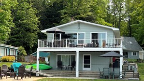 Uma casa de dois andares com varanda, área de estar externa e um gramado verde.