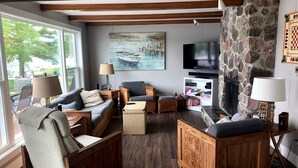 Uma sala de estar acolhedora com mobiliário de madeira, parede de pedra, televisão e um quadro de barcos.