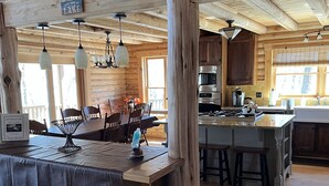 Interior rústico de una cabaña con zona de comedor de madera, cocina y asientos tipo bar.