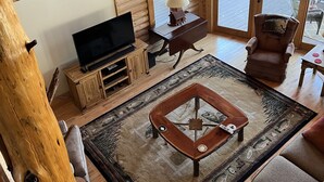 Acogedor interior de una cabaña de madera con televisor, sofá y mesa de centro.