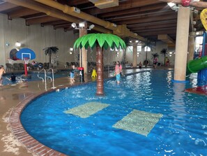 An indoor swimming pool with a central water feature resembling a palm tree, surrounded by a brick border.