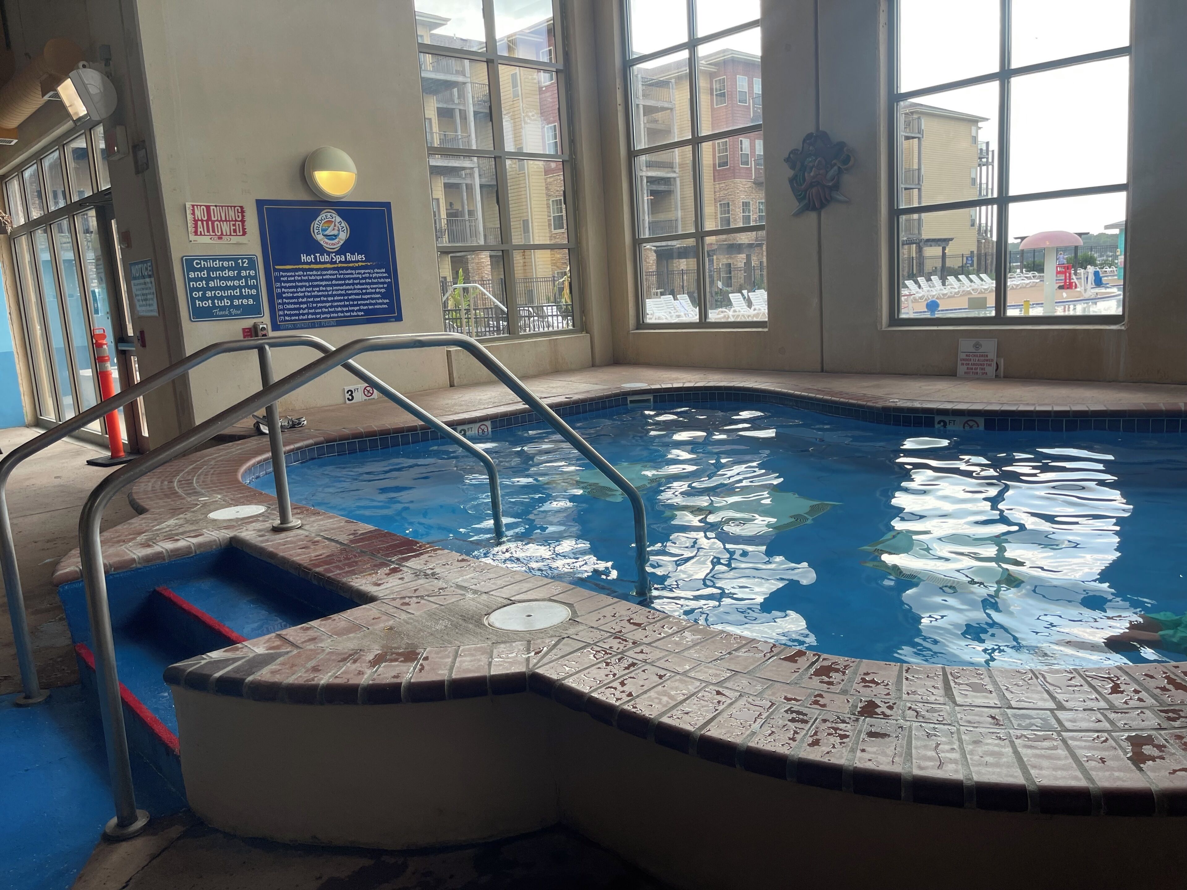 Una piscina interior con borde de azulejos, barandilla metálica y cartel que indica prohibido bucear.