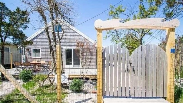 Un cancello di legno che dà accesso a una casa con portico e terrazza.