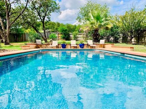Ein rechteckiger Pool mit einer bepflasterten Kante, umgeben von einer Holzdielen-Terrasse.