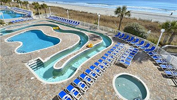 A pool area with multiple pools and lounge chairs, surrounded by a beach and ocean view. - Beautiful oceanfront condo - Bay Watch Unit 338 (North Myrtle Beach)