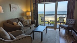 A living room with a sofa, armchairs, a coffee table, and a view of the ocean through a sliding glass door. - Beautiful oceanfront condo - Bay Watch Unit 338 (North Myrtle Beach)