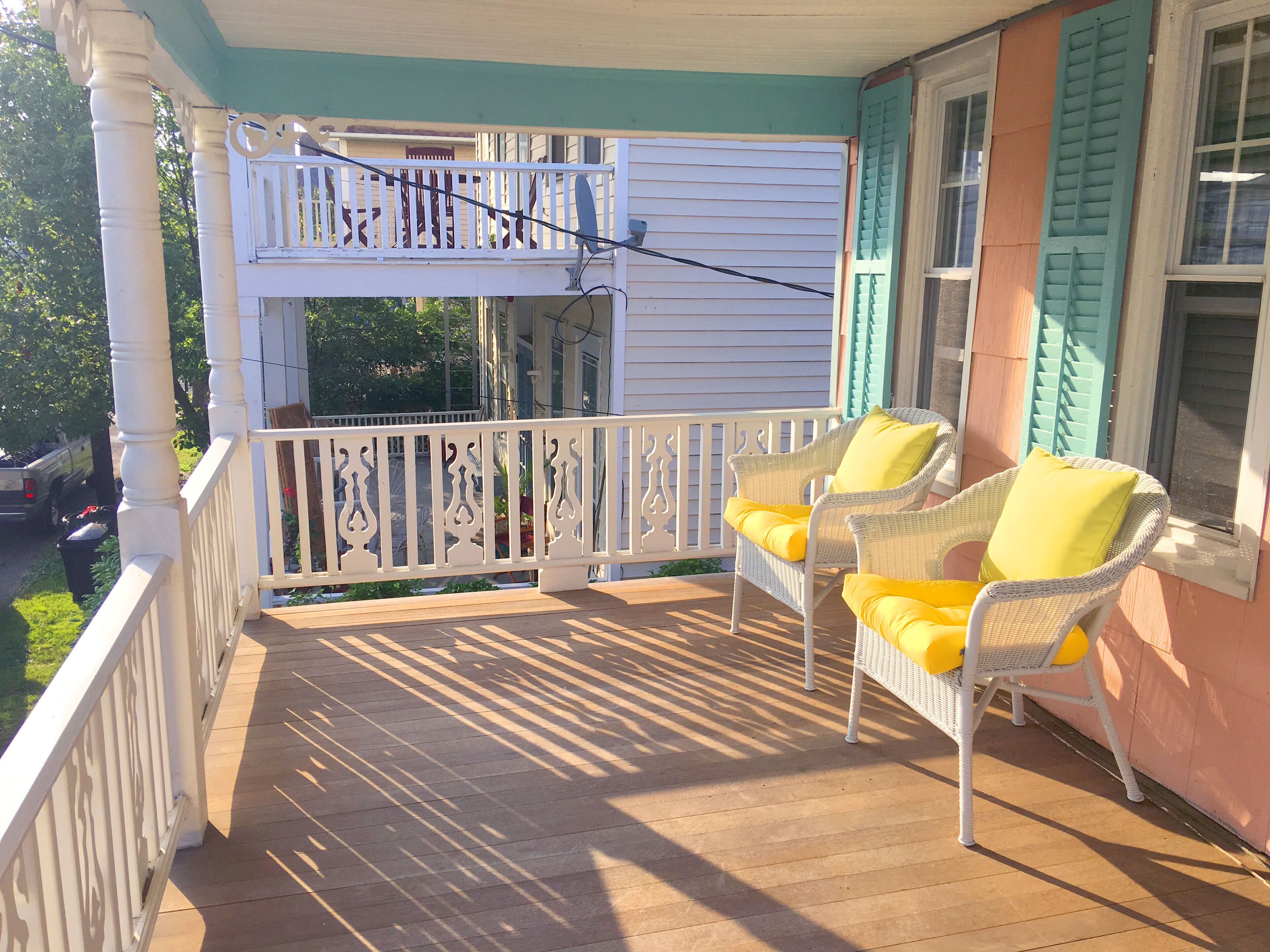 A covered porch with two wicker chairs and a white railing.