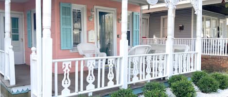 A pink building with white porch railings and blue shutters, featuring a white chair and a small white table.