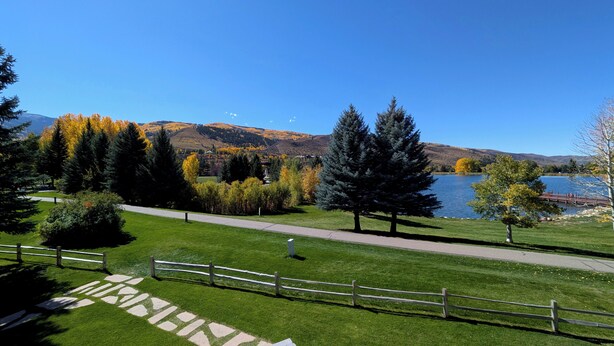 Ein Park mit einem gepflasterten Weg, einem Holzzaun und einem See mit Bergen im Hintergrund.