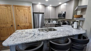 Eine Küche mit Granit-Arbeitsplatten, Edelstahlgeräten, Holzschränken und einer Bar mit Hockern.