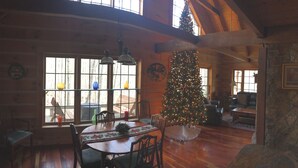A cozy cabin interior with a wooden dining table, chairs, a Christmas tree, and a large window with a view of trees. - Very private luxury log home - Now with free 5G Wi-Fi! (Millboro)