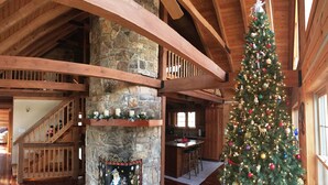 A rustic interior with a stone fireplace, wooden beams, a staircase, and a decorated Christmas tree. - Very private luxury log home - Now with free 5G Wi-Fi! (Millboro)