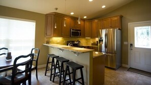 A kitchen with wooden cabinets, stainless steel appliances, a central island with stools, and recessed ceiling lights. - 3BR/2BA Lakefront Property, Includes Boat Slip (Osage Beach)