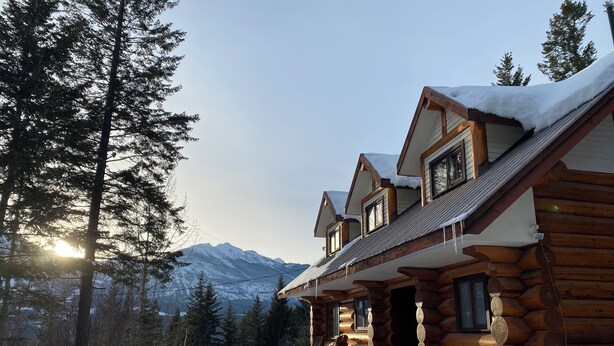 Una baita di legno con tetto innevato e vista sulle montagne sullo sfondo.