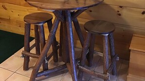 Ein rustikaler Holztisch mit einer Radkonstruktion an der Rückenlehne, begleitet von zwei Hockern.