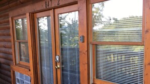 Eine Holzhütte mit der Nummer „8472“ über dem Eingang, einer Tür mit Glasfenster und einem Fenster mit Rollläden.