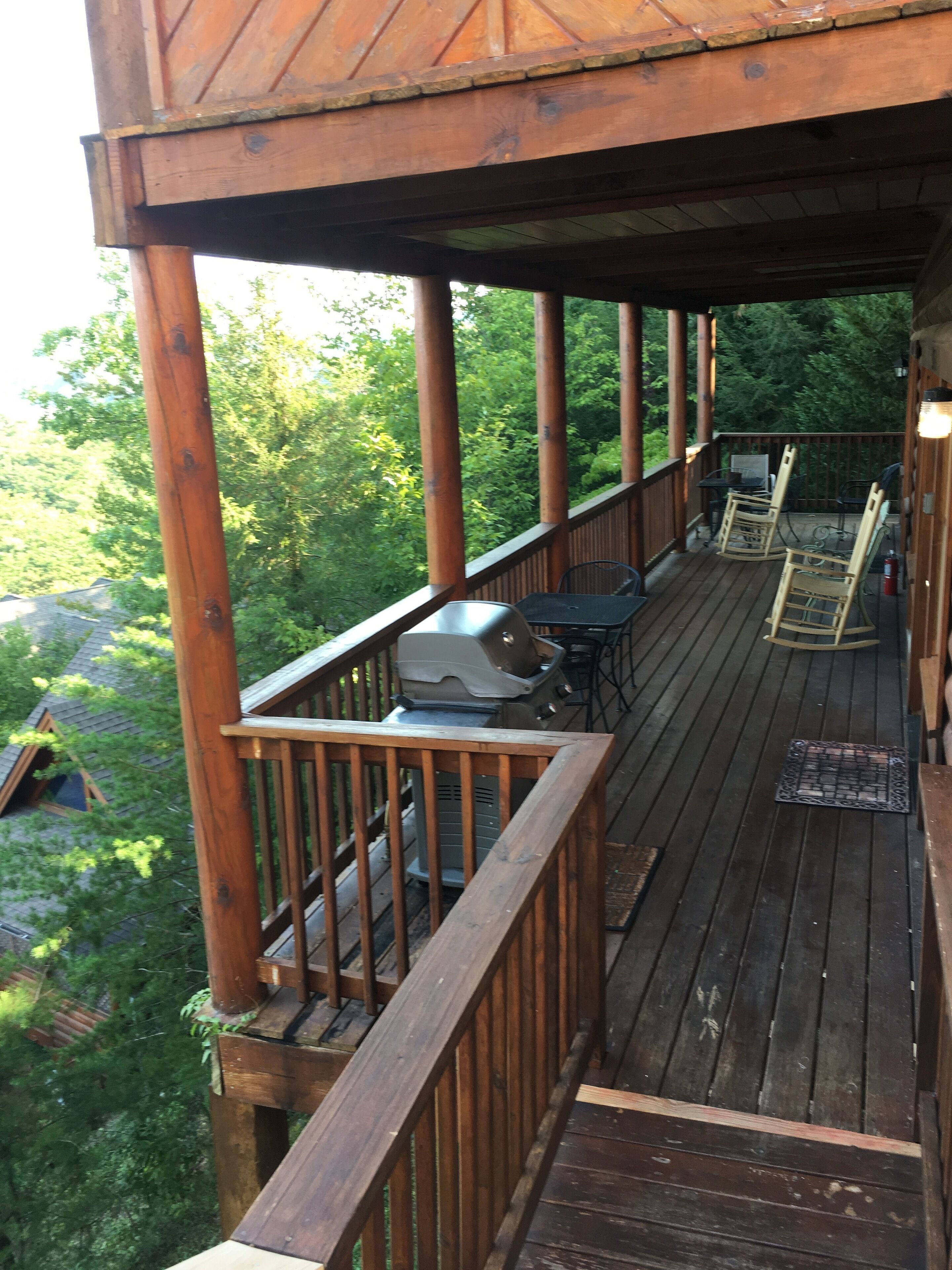 Une terrasse en bois avec un barbecue, deux chaises et une table.