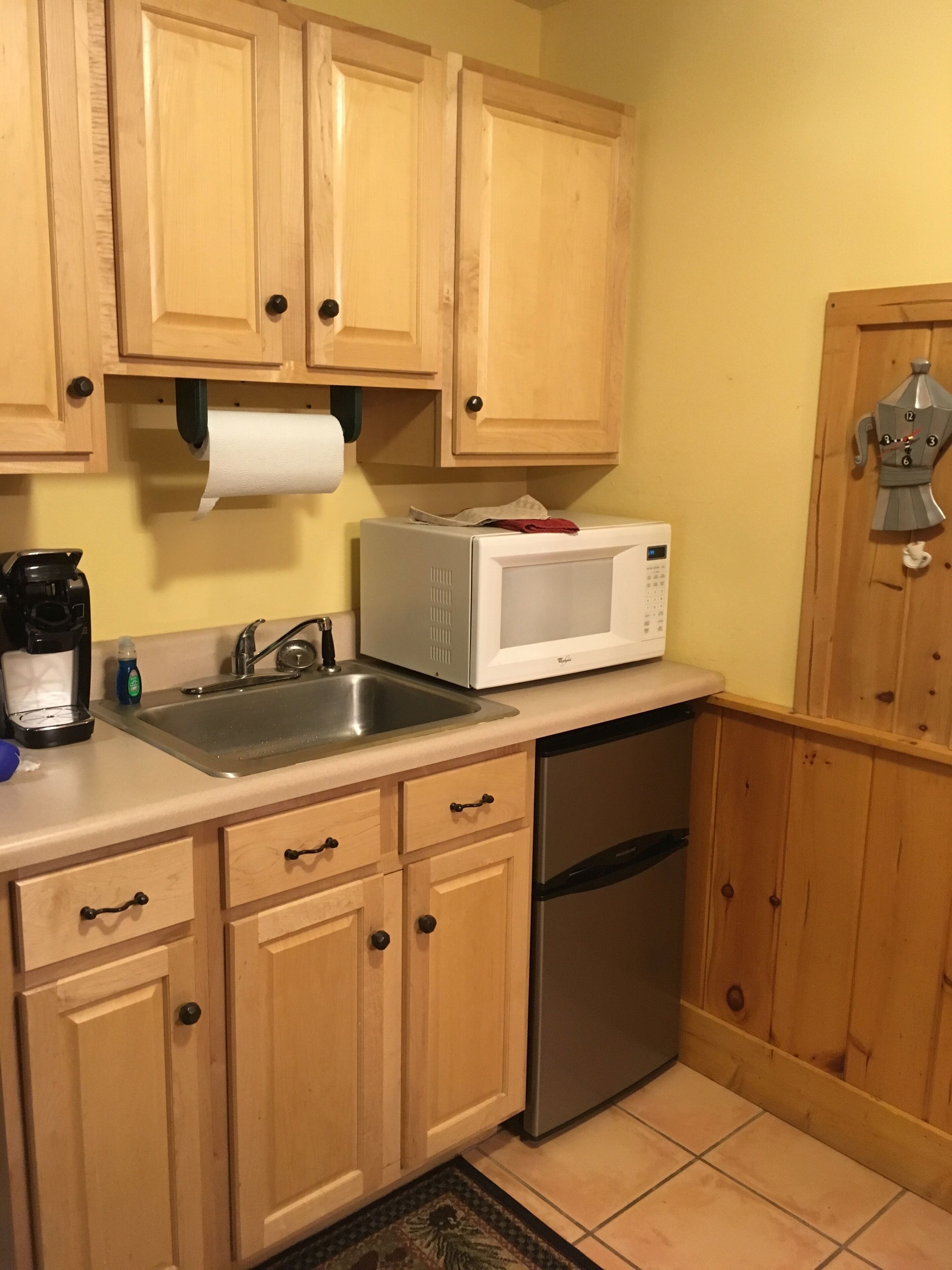 Una cocina con armarios de madera, un lavamanos de acero inoxidable, un microondas blanco y un lavavajillas.