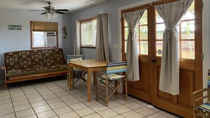A room with a sofa, a table, chairs, a ceiling fan, and a door with curtains. - HALE NIHI, Paia, Maui (Paia)