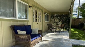 A covered patio area with a wicker sofa, a table, and chairs. - HALE NIHI, Paia, Maui (Paia)