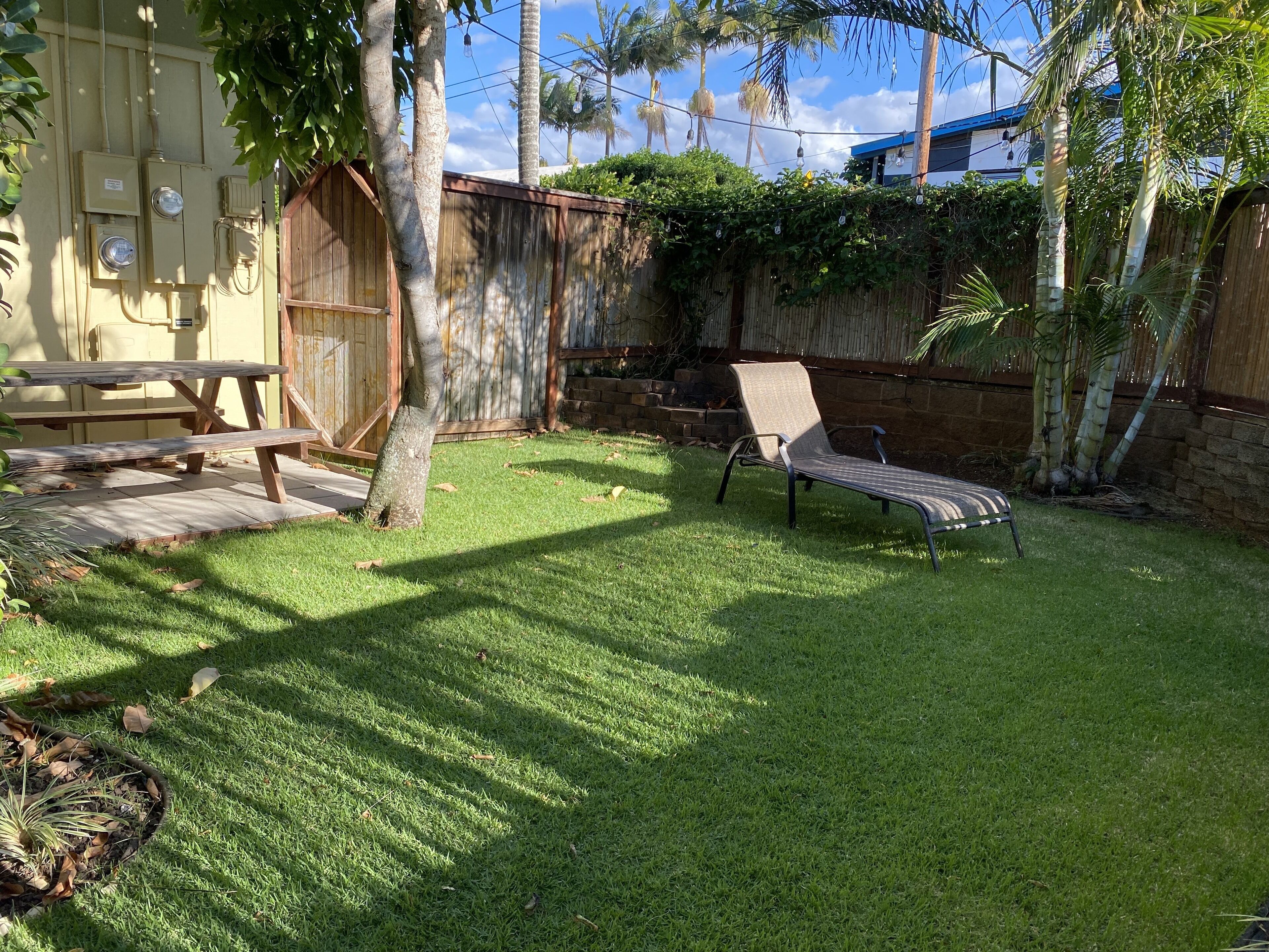 A backyard with a wooden bench, a lounge chair, and a picnic table.