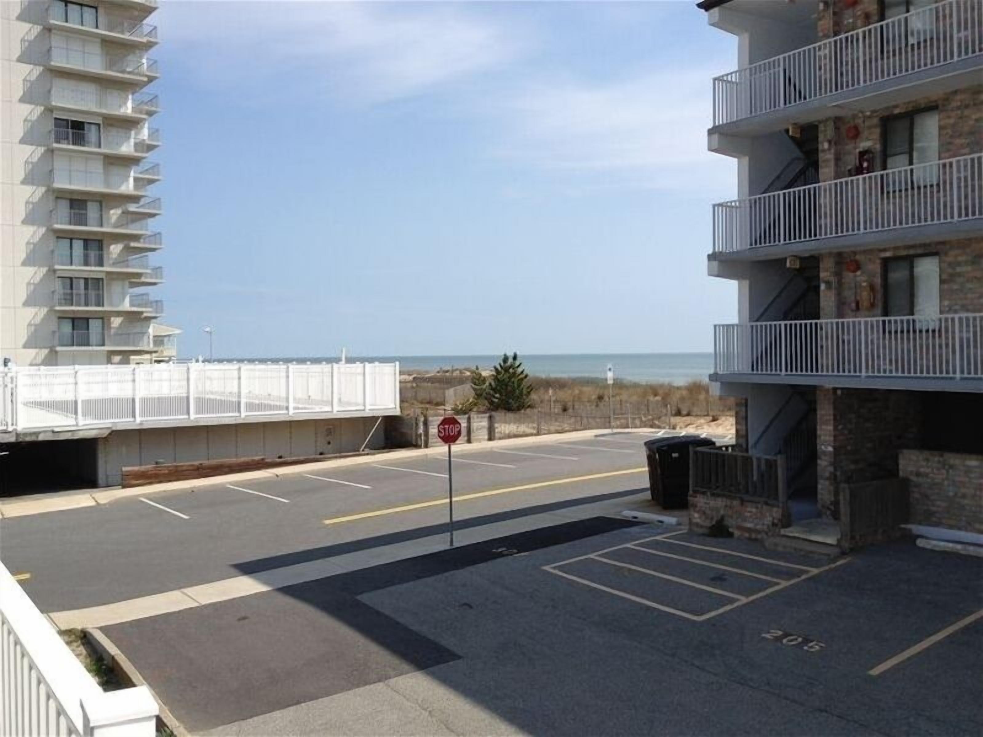 Un parking avec un panneau de signalisation, un immeuble doté de balcons et une vue sur la plage.