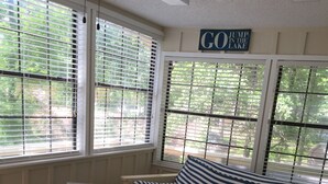 A cozy room with a striped sofa, a small table with photos, and large windows with blinds. - Almost Seaside - Waterfront Paradise On Cedar Creek Lake! (Gun Barrel City)
