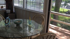 A dining area with a glass table surrounded by wicker chairs, a bowl of fruit, and a decorative item on the table. - Almost Seaside - Waterfront Paradise On Cedar Creek Lake! (Gun Barrel City)
