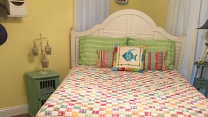 A bedroom with a quilted bedspread, a green skirted bed, a white headboard, a small green nightstand, and a wall-mounted shelf. - Almost Seaside - Waterfront Paradise On Cedar Creek Lake! (Gun Barrel City)
