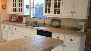 A kitchen with white cabinets, a tiled countertop, a sink, and a coffee maker. - Almost Seaside - Waterfront Paradise On Cedar Creek Lake! (Gun Barrel City)