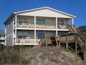 Ein Strandhaus mit zwei Etagen, jeweils mit Balkon, einer Holzterrasse und einer Treppe zum Obergeschoss.