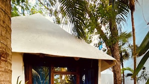 A small, single-story building with a white exterior and a large window. There are two wooden stools in front of the window, and the ground is covered with pebbles. - MIO Tulum Hotel Boutique (Tulum)