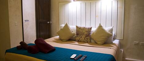 A hotel room with a bed, pillows, a blue blanket, and remote controls.