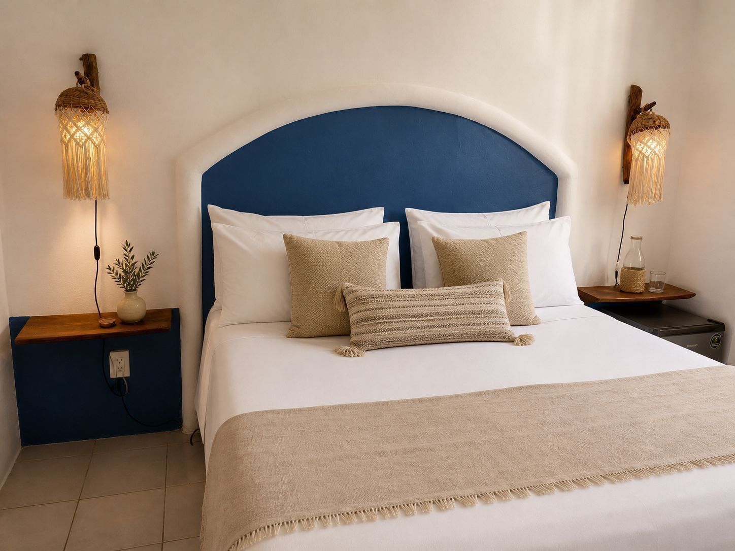 A neatly made bed with a blue headboard, two bedside tables with lamps, and a small plant on the left table.