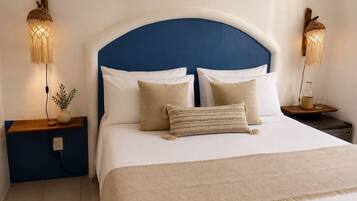 A neatly made bed with a blue headboard, two bedside tables with lamps, and a small plant on the left table.