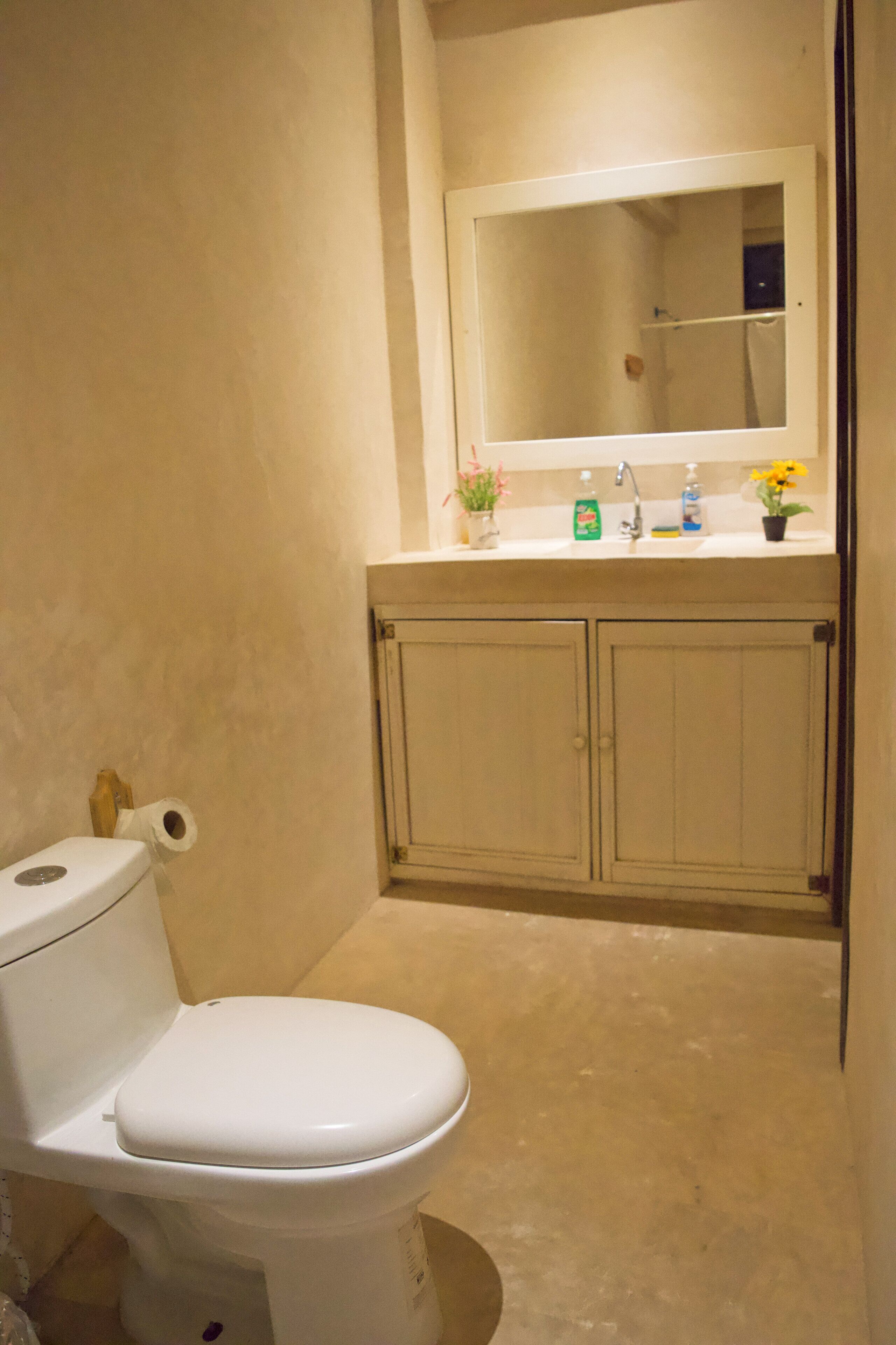 Une salle de bain avec des toilettes, un lavabo avec un miroir au-dessus et des placards en dessous.