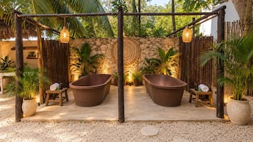 Uma área de spa com duas banheiras grandes, parede de pedra e plantas tropicais.