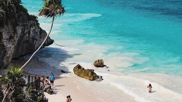 A beach with clear turquoise water, palm trees, and people enjoying the shore. - MIO Tulum Hotel Boutique (Tulum)