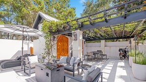 Un patio al aire libre con mobiliario moderno, una chimenea y una pérgola.