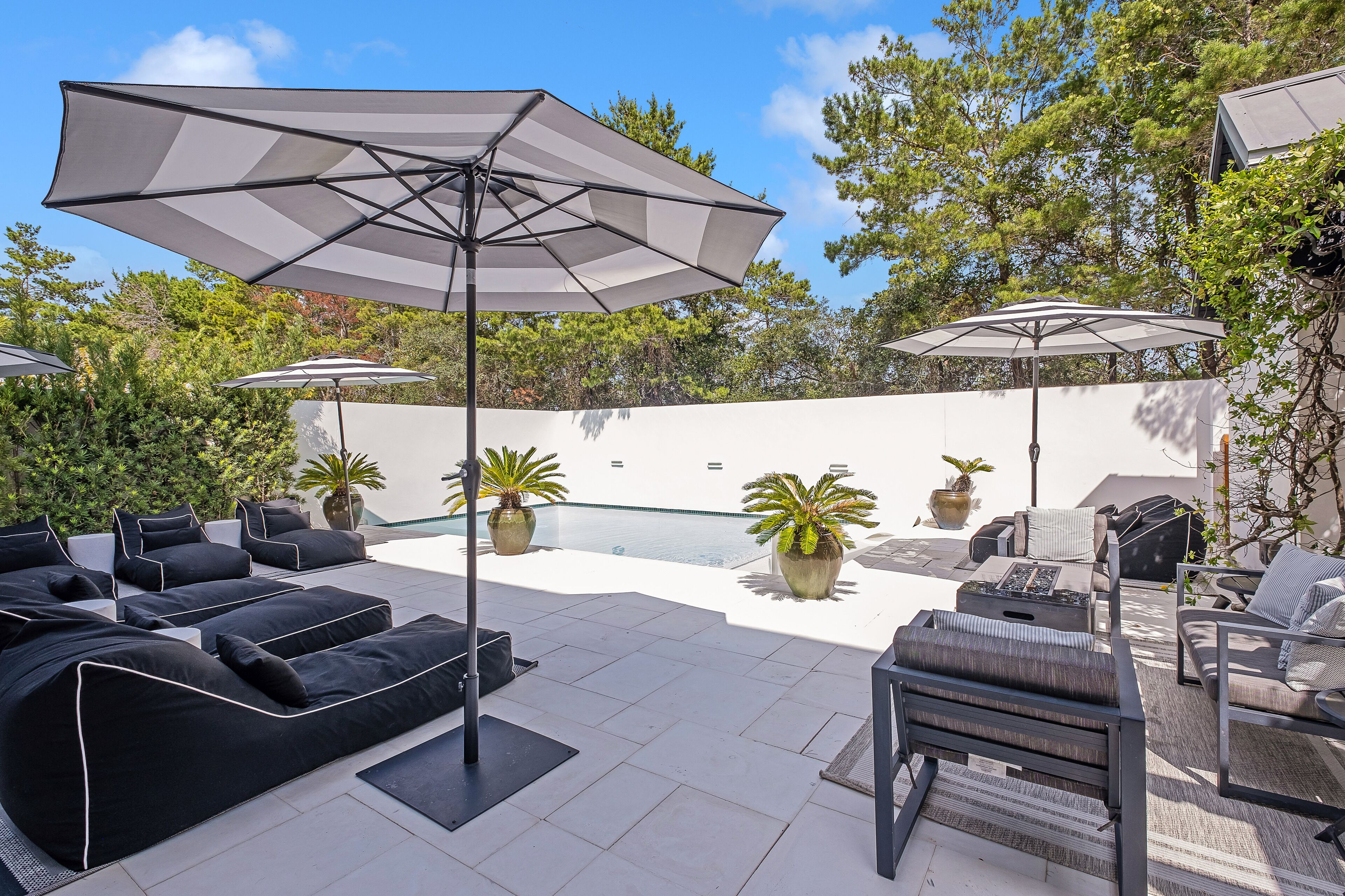 A modern outdoor patio with black and white furniture, including sofas and chairs, and large umbrellas providing shade.