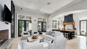 Amplia sala de estar con chimenea, muebles blancos y una cocina con una isla grande.