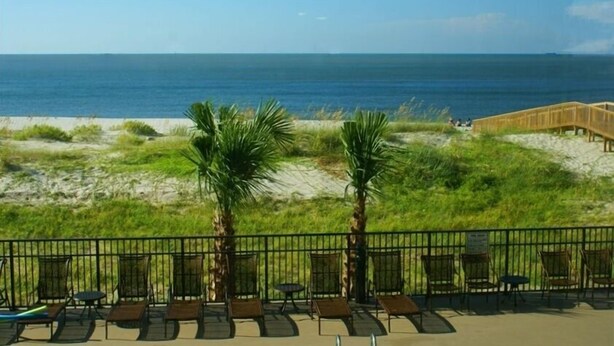 Blick auf einen Strand mit einer Holzpromenade, Liegestühlen und einer Palme.