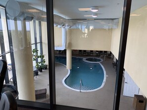 An indoor swimming pool with a hot tub, surrounded by seating areas and potted plants.