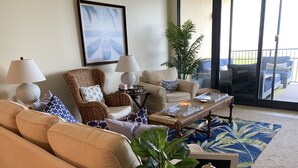 Ein Wohnzimmer mit einem beigefarbenen Sofa, einem Korbstuhl, einem Couchtisch und einer Topfpflanze.