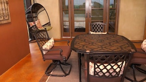 A dining area with a round table and four chairs, a hanging chair, and a view through glass doors.