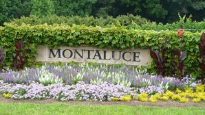 A sign reading "MONTALUCE" with a garden in the foreground featuring various flowers and a stone wall.