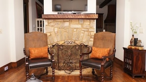 A living room with two leather armchairs, a stone fireplace, and a television mounted above it.