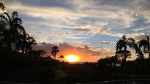 A sunset over a body of water with palm trees and a building in the background.
