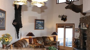 A living room with a fireplace, mounted animal heads, and a large window. - On Rainbow Lake, 3 bedroom 2 1/2 baths/Free WiFi, 65 inch tv, Pinetop-Lakeside. (Pinetop- Lakeside)